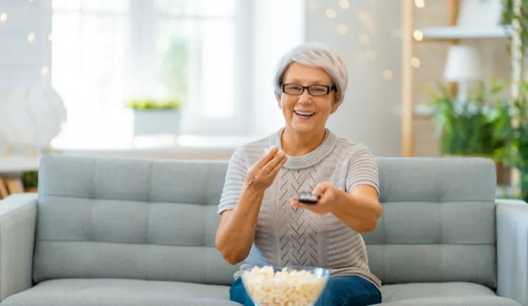 lady turning on the tv with a remove smiling and eating popcorn