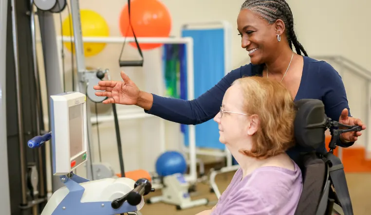 older lady using machinery for rehab with nurse guidance