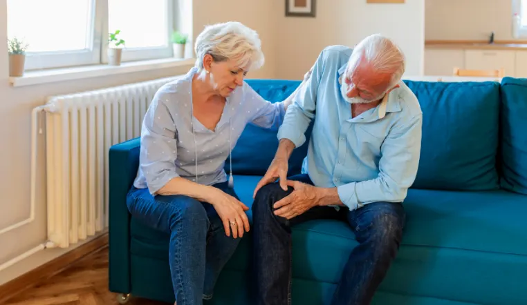 man touching his knee in pain while loved one is there to comfort him