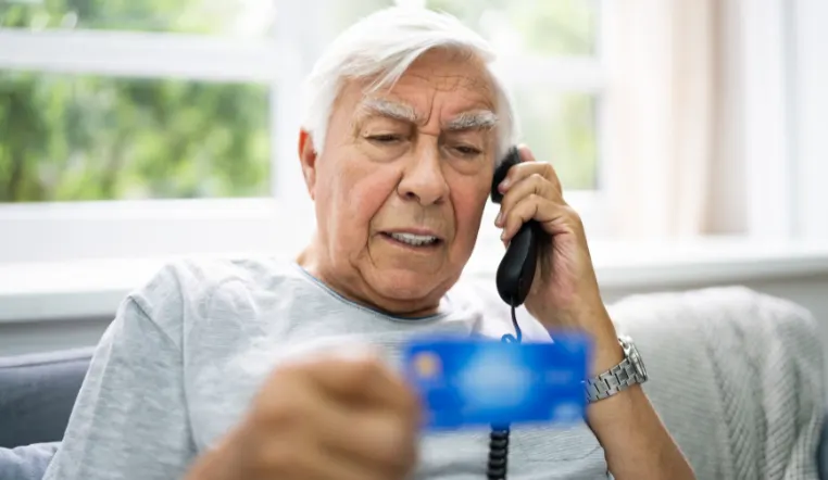 older man on the phone looking at bank card