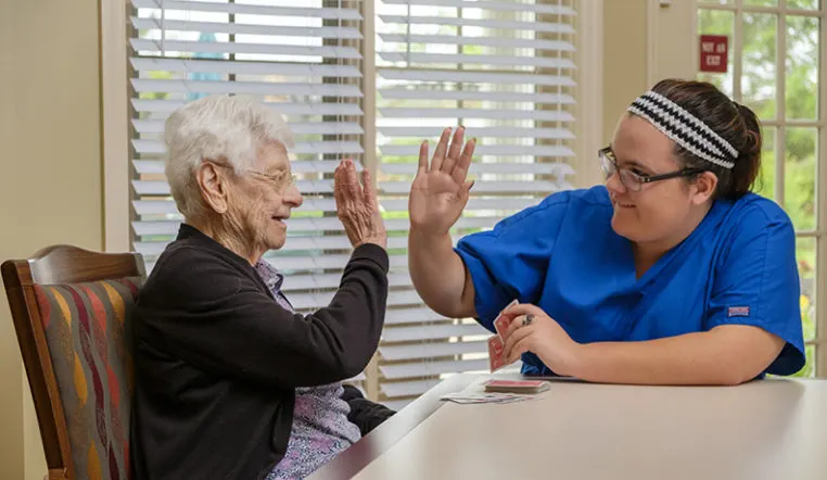 staff and resident smiling at each other giving high fives while playing cards