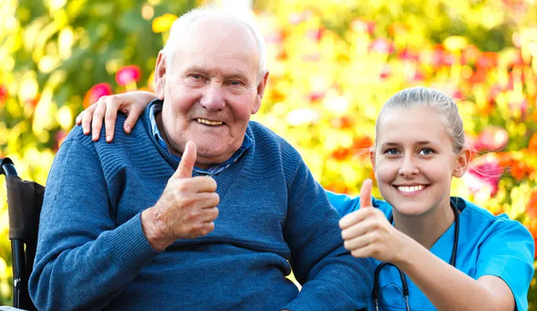 nurse and senior smiling at camera with thumbs up