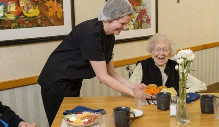 senior at dining table getting food served to her by staff