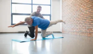 senior man doing yoga poses with help from staff
