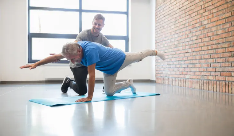 senior man doing yoga poses with help from staff