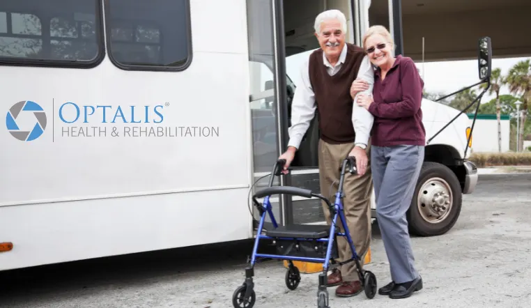 senior couple smiling at camera outside of a transportation bus for seniors