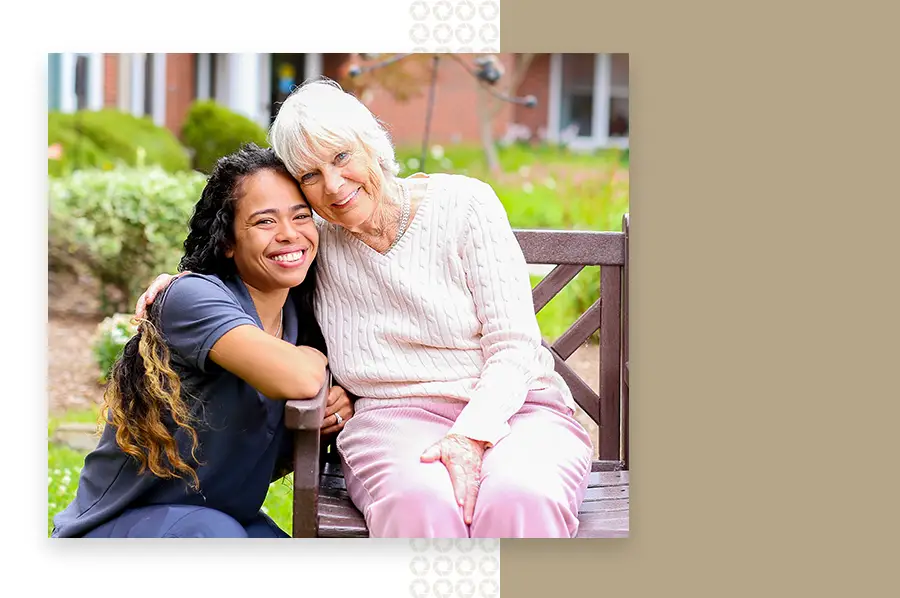 Senior woman in pink smiles and puts her arm around young nurse