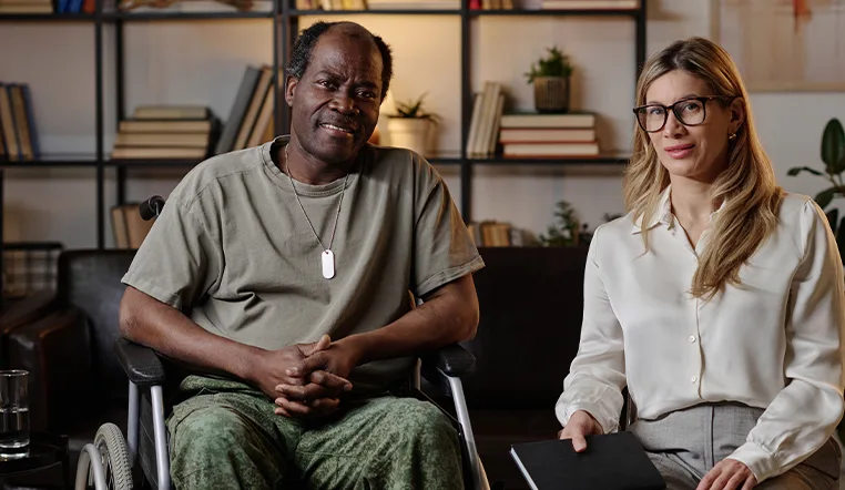 Veteran in wheelchair next to professional woman holding a notebook